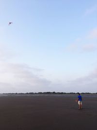 Rear view of man flying kite on land against sky