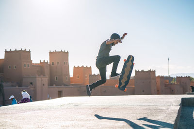 Side view of man performing stunt on skateboard against castle during sunny day