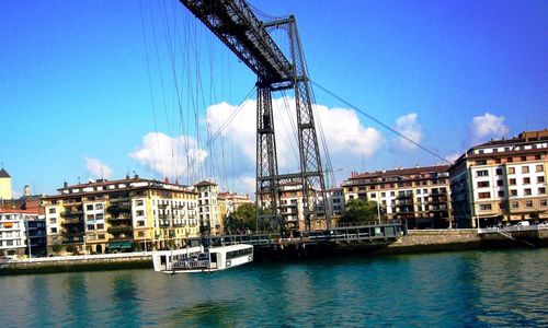 Boats in river by cityscape against blue sky