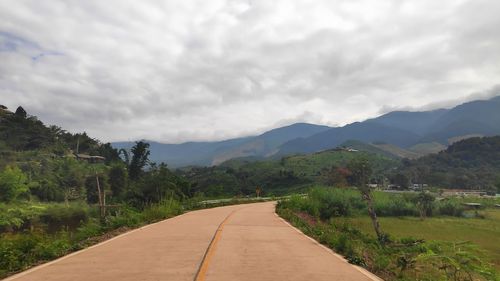 Empty road leading towards mountains against sky