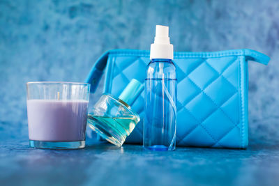 Close-up of small spray bottle with clutch bag and candle on blue table