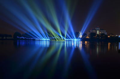 Illuminated lights by river against sky at night