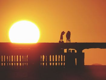 Silhouette people standing by sea against orange sky