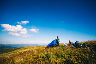 People sitting on field against blue sky