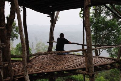 Rear view of man sitting on wood in forest