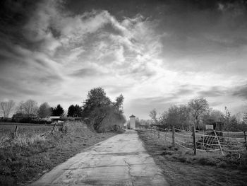 Footpath amidst trees on field against sky