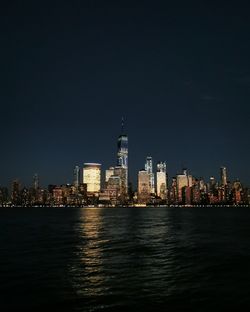 Sea by illuminated buildings against sky at night