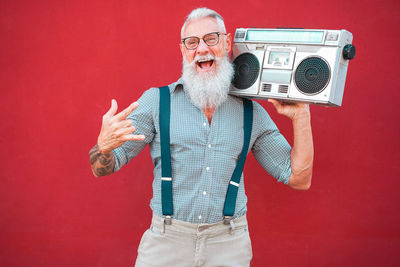 Portrait of bearded man holding radio while standing against red background