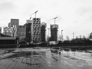 Buildings by wet street against sky in city