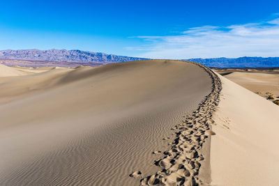 A foot path in the sand, running along the top of a sand dune in death valley national park.