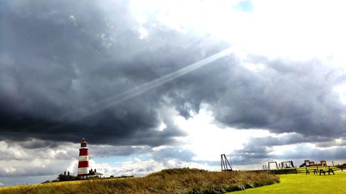 Lighthouse on landscape against cloudy sky