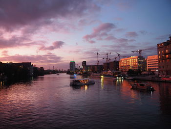 River by illuminated buildings against sky at sunset