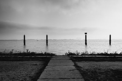 Narrow jetty leading to calm sea against the sky