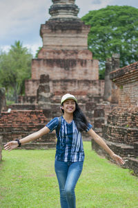 Full length of young happy woman standing against historical park.