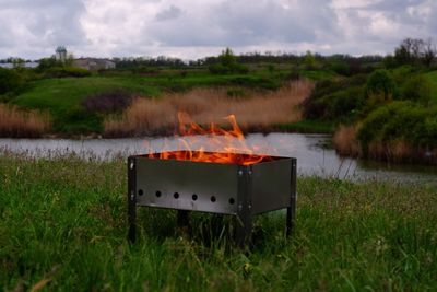 Fire burning in pit on grass against sky