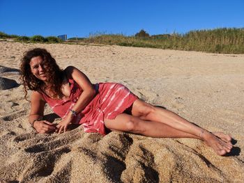 Young woman lying on sand at beach against sky
