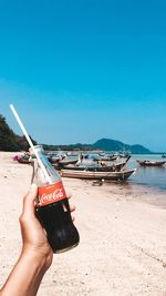 Hand holding umbrella on beach against clear blue sky