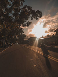 Road by trees against sky during sunset