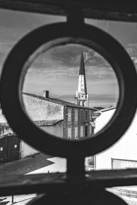 Tower by buildings against sky seen through glass