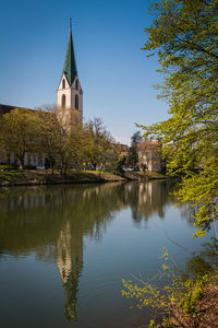 Reflection of building and trees by lake against sky