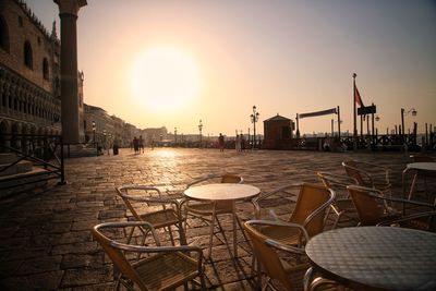 Chairs in city against sky at sunset