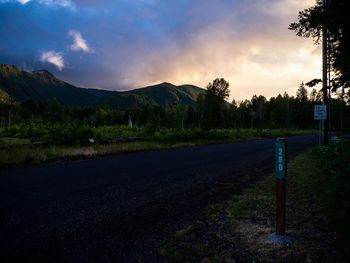 Road by trees against sky during sunset