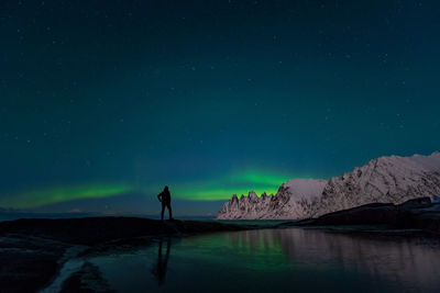 Rear view of man standing against aurora borealis at night