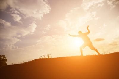 Silhouette woman with arms raised against sky during sunset