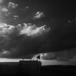 Low angle view of bird perching on building against cloudy sky