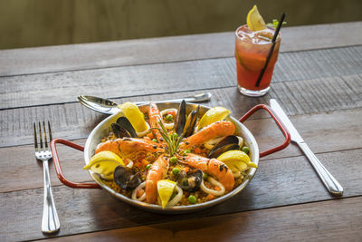 High angle view of paella served in bowl with drink on wooden table