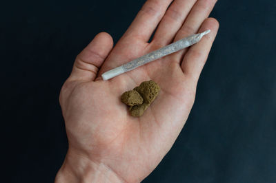 Close-up of hand holding cigarette over black background