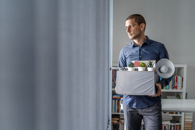 Businessman holding cardboard box looking away in office