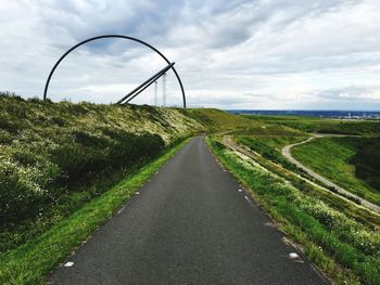 Horizon observatory on field by road against cloudy sky