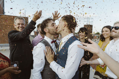 Loving gay couple kissing and guests throwing confetti during ceremony