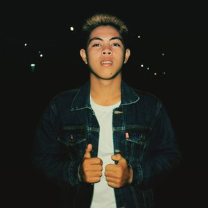Portrait of young man standing against black background
