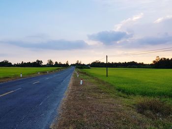 Empty road amidst field against sky during sunset