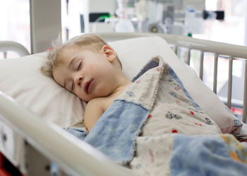 Toddler sleeps on back in hospital bed.