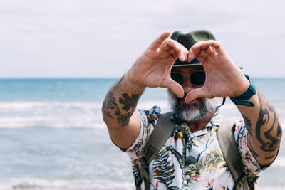 Smiling man making a heart shape with his hands on the beach