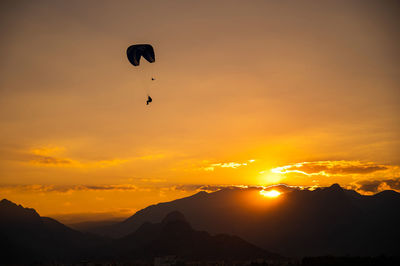 Silhouette people paragliding against sky during sunset