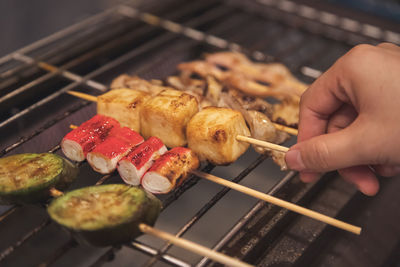 Hand holding one of fish meatball in stick grilling on the stove with other meatball type