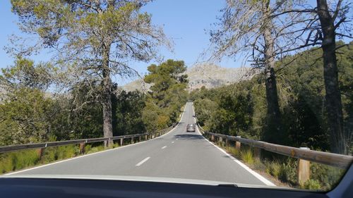 Road amidst trees against sky seen through car windshield