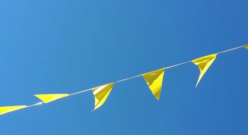 Low angle view of flags hanging in row against clear blue sky