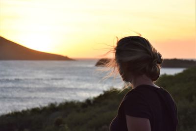 Rear view of woman looking at sea during sunset