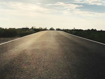 Empty road amidst field against sky