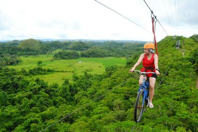 Woman riding bicycle on rope over landscape