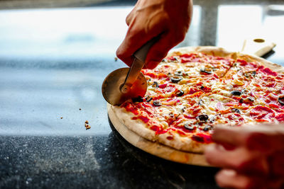 Close-up of person cutting pizza at restaurant