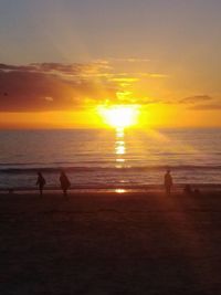 Silhouette people on beach against sky during sunset