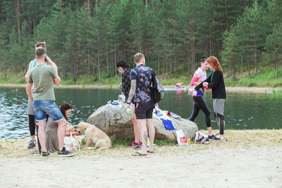 Rear view of people with dogs on shore against trees