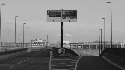 Road sign on highway by street against sky