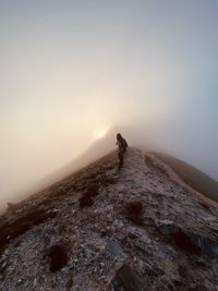 Man standing on rock against sky during foggy weather